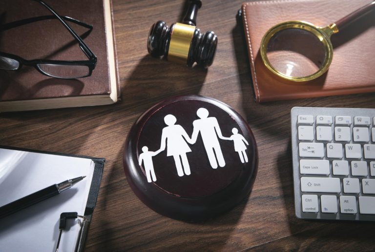 A wooden block with a family icon, a gavel, magnifying glass, notebook, glasses, pen, and keyboard on a wooden desk, representing Affordable Family Law Attorneys and Family Law Houston services.