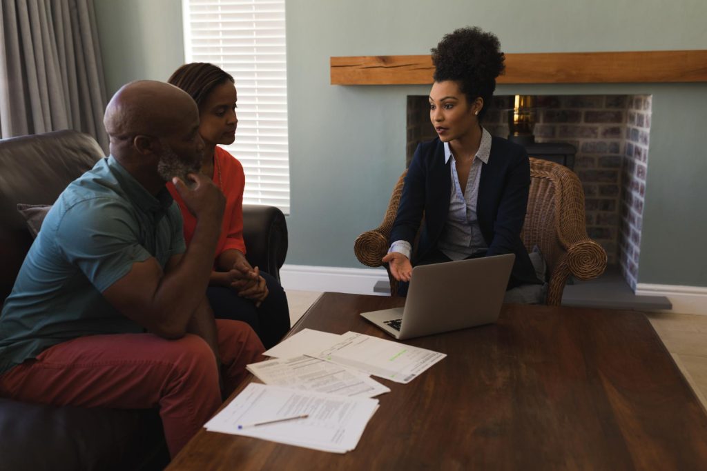 Three people sit in a living room having a discussion; papers and a laptop are on the table in front of them, as African American family law attorneys help guide their conversation.