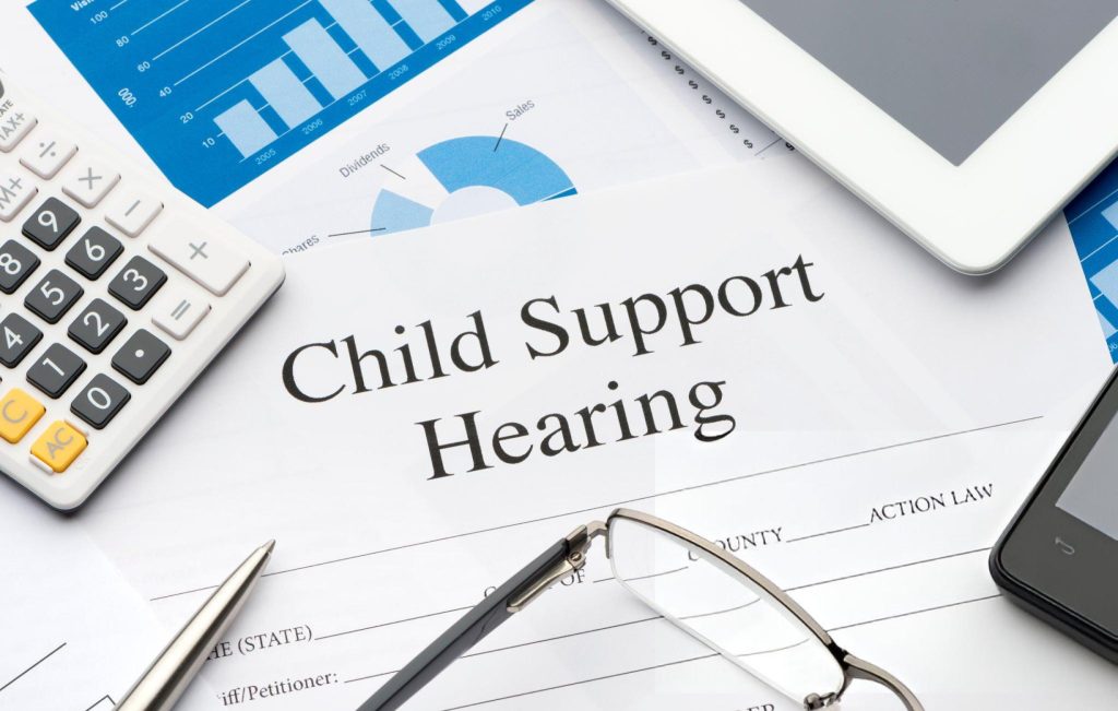A document titled "Child Support Hearing" on a desk with a calculator, eyeglasses, charts, a smartphone, and a tablet—representative of Texas Child Support proceedings.