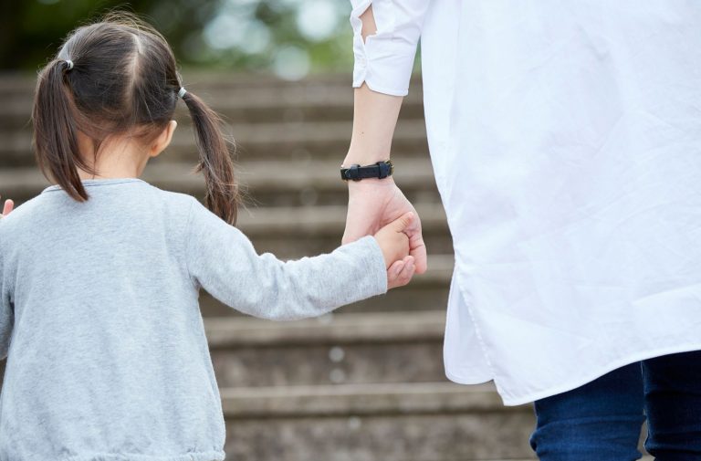 A young girl holding an adult's hand while walking up outdoor steps in Houston, photographed from behind.
