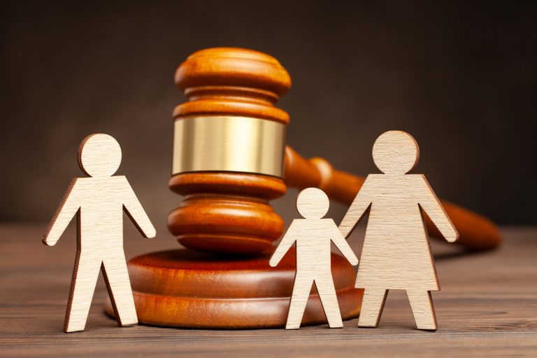 Wooden cutouts of a family stand in front of a judge's gavel, symbolizing legal decisions such as Texas child custody or standard custody agreements.