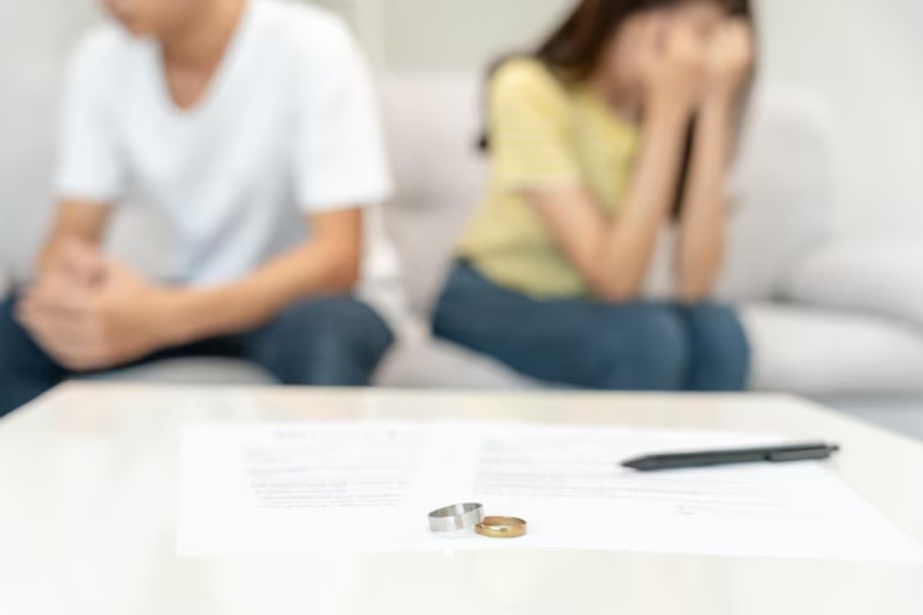 A man and woman sit apart on a couch with rings and paperwork on the table in front of them, highlighting divorce mediation challenges and the importance of financial mediation during separation.