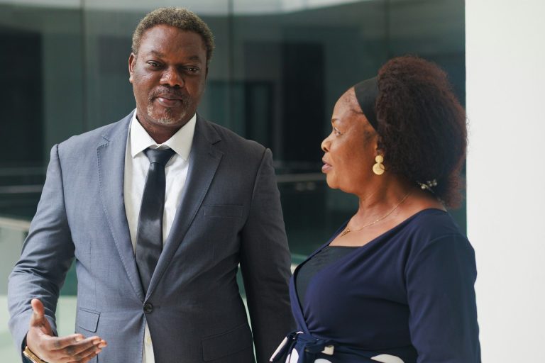 Two professionally dressed people, a man in a suit and a woman in a dark dress, converse indoors near a white pillar—reflecting the professionalism you can expect from Black Divorce Attorneys Houston.