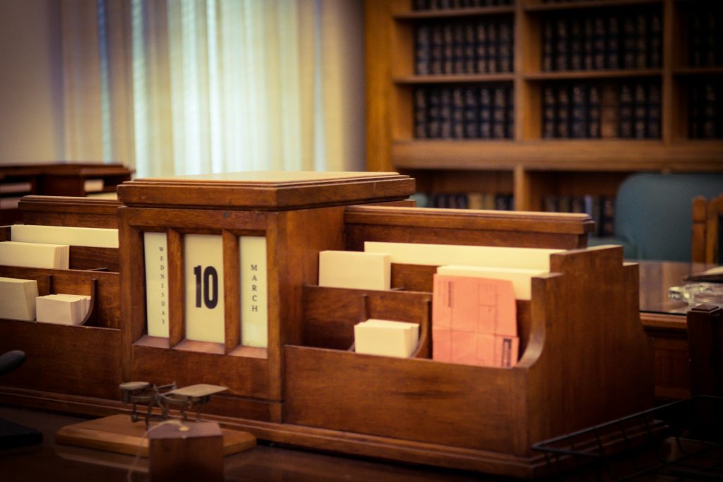 A wooden desk organizer holds paper files and a perpetual calendar displaying "10 March" in a library or office, highlighting the unique contributions of Black divorce attorneys with bookshelves in the background.