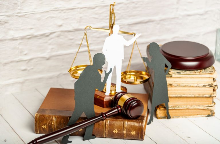 Paper cutouts of people stand next to a gavel, scales of justice, and old books, symbolizing a legal or courtroom scene often navigated by a Board Certified Family Lawyer.