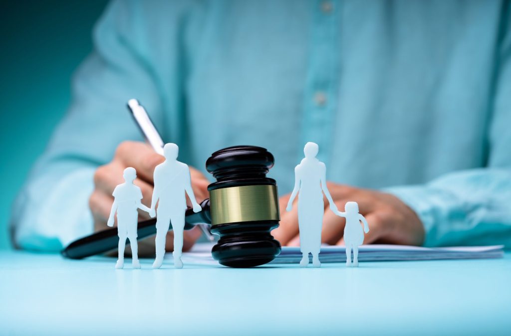 A gavel on a desk with paper cutouts of families, while a Board Certified Family Lawyer in the background writes on a document.