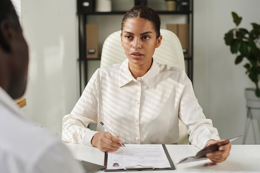 A woman in a white shirt holds a passport and fills out a form while discussing her case with one of the top female divorce lawyers in an office setting.