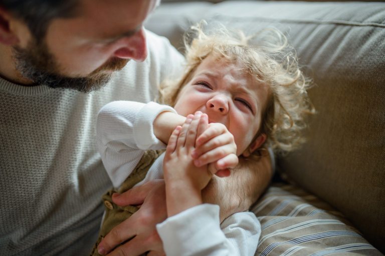An adult holds a young child who is crying and covering their mouth with their hands while sitting on a couch, capturing the emotional moments often seen in child custody Texas situations.