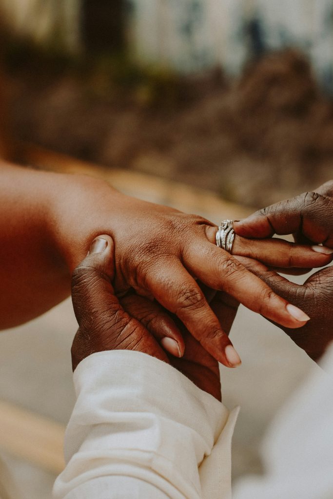 Close-up of one person placing a silver ring on another's finger, both in light-colored clothing, symbolizing the start of their marriage and perhaps the conversations about a prenuptial agreement.