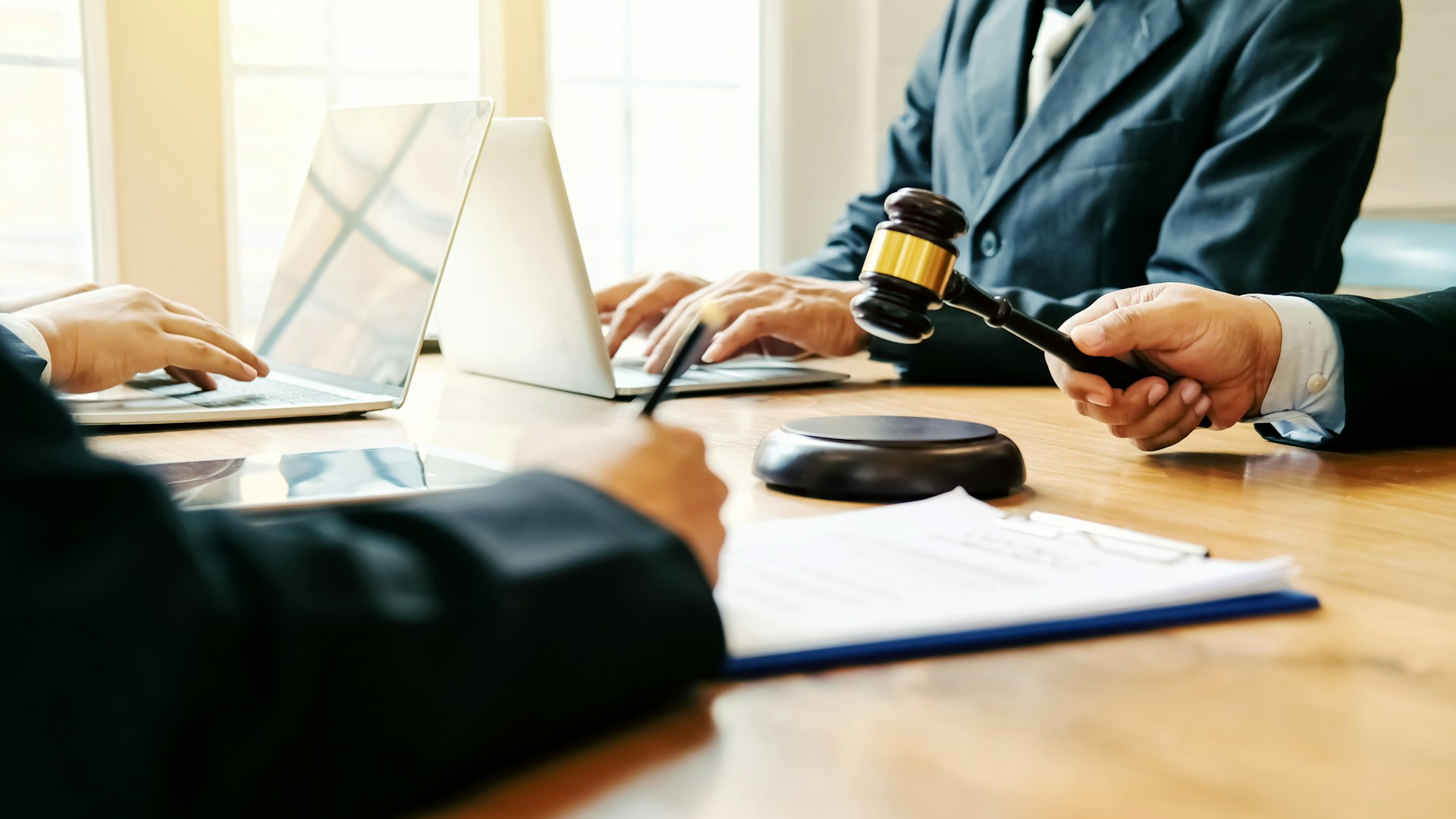 Three people in business attire sit at a table with laptops and documents, discussing the benefits of financial mediation as one person hands a judge’s gavel to another.