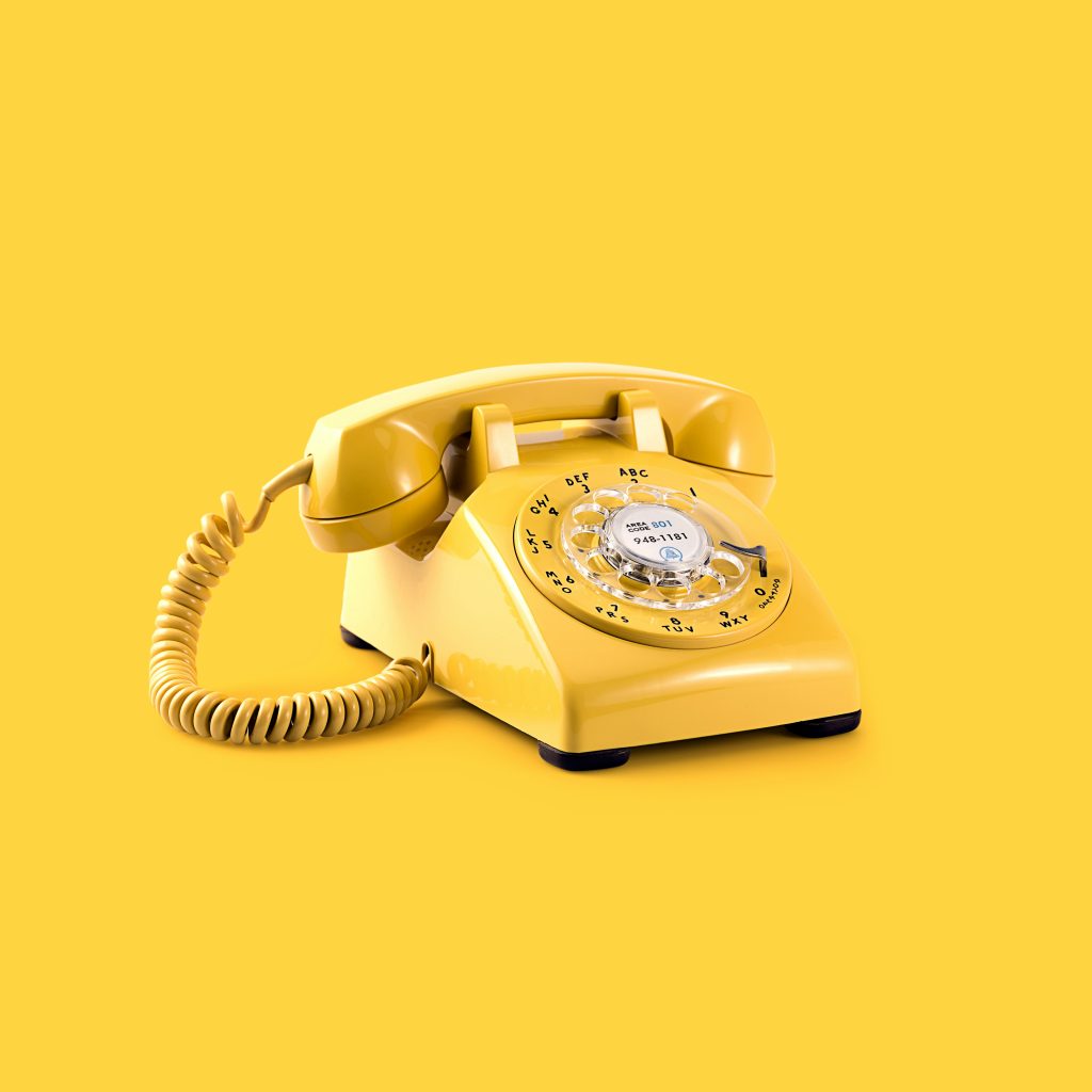 A yellow rotary dial telephone with a coiled cord sits against a solid yellow background, symbolizing how mediation can help you protect yourself with clear communication.