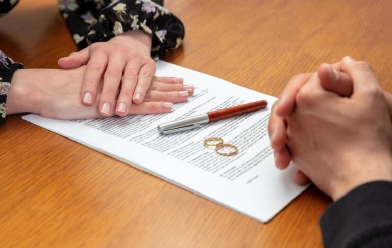 Two people sit across a table with hands folded on a document, a pen, and two wedding rings placed on the paper, symbolizing their consideration of premarital agreements as they guide each other through important decisions in Texas.