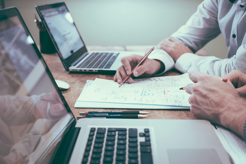 Two people working at a desk with laptops and paperwork, discussing and taking notes with pens as they review a guide for couples seeking a peaceful divorce through mediation.