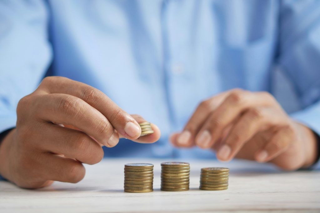 A person in a blue shirt stacks piles of coins on a white table, organizing and counting Texas child support payments.
