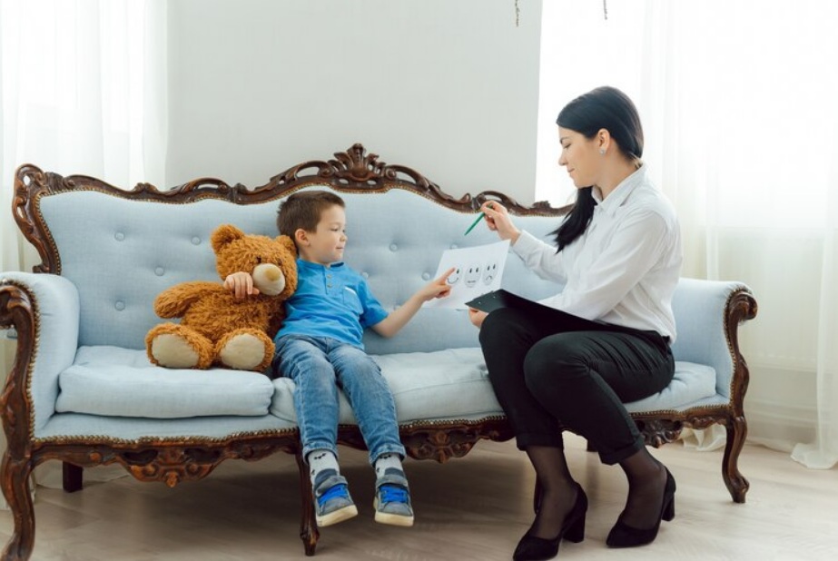 A woman shows flashcards to a young boy holding a teddy bear while sitting together on a blue couch, highlighting quality moments often seen during Texas child visitation schedules in a bright room.