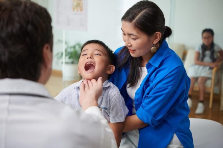 A doctor examines a young boy’s throat while he sits on his mother’s lap in a medical office, where families might also seek guidance on Texas laws and visitation rights.