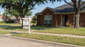 For Sale sign posted in front yard of brick residential home