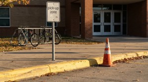 School pick-up zone sign with traffic cone near bike rack entrance