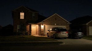 Two vehicles parked in driveway outside brick house with porch light at night